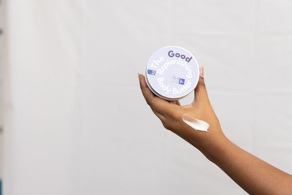 A hand holding a replenishing body butter container, showcasing skincare.