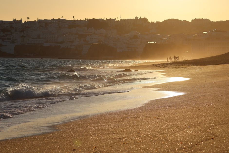 A serene beach scene at sunset with silhouettes and gentle waves.